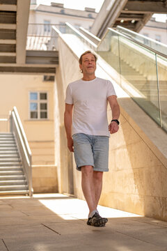 55 year old man walking along modern architecture in an urban pedestrian area during summer.