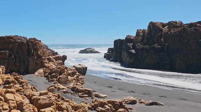Powerful sea waves crashing into a narrow rocky channel on a dark sand shore.