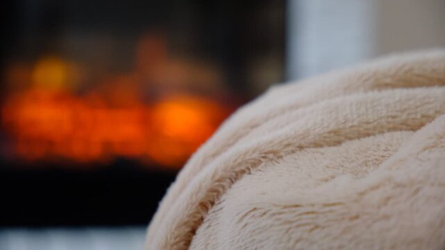 Fireplace and fluffy warm beige blanket. Autumn whispers through the window, while inside, warmth and comfort reign supreme. Snuggled under a soft, warm blanket by the crackling fireplace