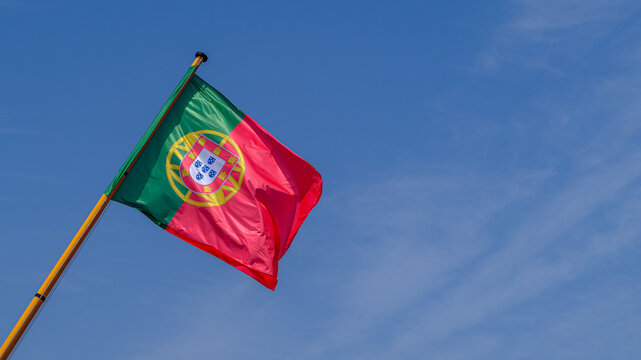 Wehende portugiesische Flagge an einem Fahnenmast aus Holz im Wind vor blauem Himmel mit Textfreiraum