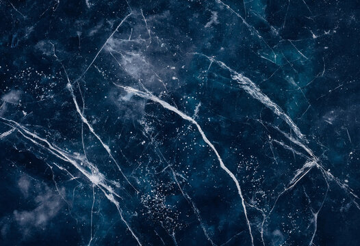 Close up of dark blue ice texture with intricate white cracks and frozen air bubbles trapped beneath the surface of a frozen lake in winter