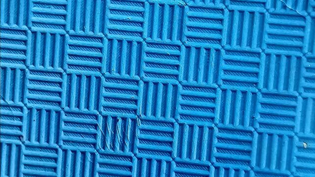 Close-up shot of a textured blue rubber mat with a grid pattern. Abstract background with geometric lines and non-slip surface texture, ideal for industrial, flooring, or design concepts.
