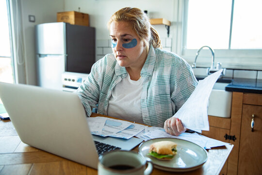 Woman paying household bills online at kitchen table