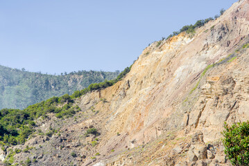 Fototapeta premium Dramatic landscape view of a steep, eroded mountain slope with exposed rocky cliffs and sparse vegetation under a clear blue sky in a rugged natural environment