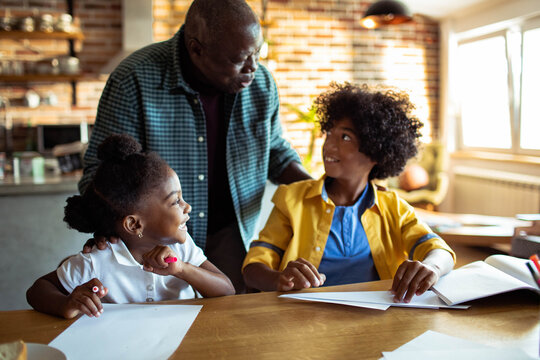 Grandfather helping grandchildren with homework at kitchen table