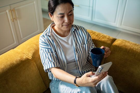 Woman using smartphone with coffee on sofa at home