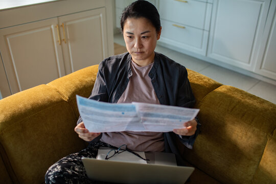 Mature woman reviewing bills at home on sofa with laptop