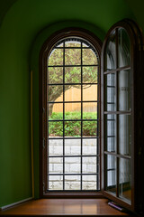 Fototapeta premium Street view with a tree and a wall from a dark green arched corridor with a lattice on the door