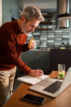 Middle-aged man multitasking at kitchen counter while working from home