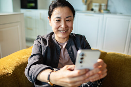Smiling woman using smartphone at home on sofa