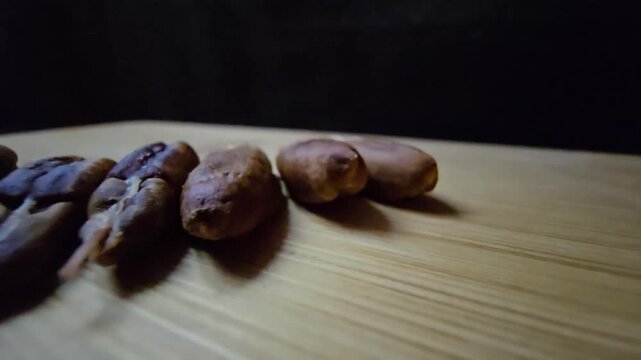 Close-up of dried date pits (seeds) arranged on a wooden board, highlighting the natural textures of palm seeds against a dark background, perfect for organic, agricultural, and culinary concepts.