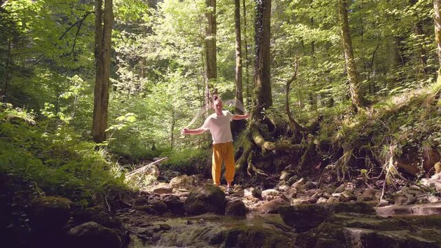 A man practices balance on a rocky stream in a lush forest, meditating among towering trees in a serene, zen-like state, embodying a healthy lifestyle through yoga and relaxation.