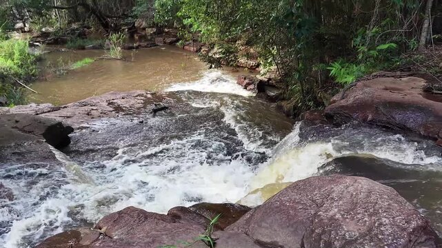V&iacute;deo de queda d'&aacute;gua natural correndo sobre pedras escuras cercada por vegeta&ccedil;&atilde;o densa de floresta tropical no Parque Nacional da Chapada Diamantina, Bahia, Brasil.
