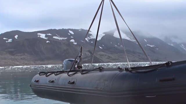Witness a critical moment of an Arctic journey as a reliable tender descends from an exploration vessel towards the tranquil, cold sea. Floating ice dots the expanse before rugged, snow-dusted peaks.