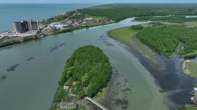 High angle drone shot of Anaklia coastal resort in Georgia, showing the famous pedestrian bridge, green river island, and scenic sea delta landscape.