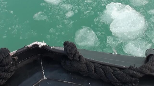 Witness the breathtaking view from a ship navigating the vast Arctic Ocean, where a tapestry of emerald water meets scattered, dazzling ice formations during a serene journey.