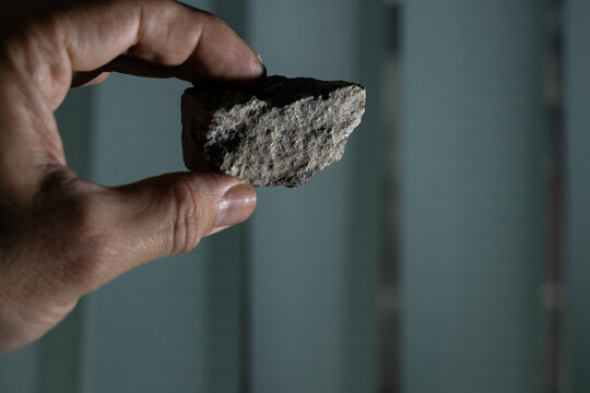 Holding a dark stone in hand; vertical window blinds in the background