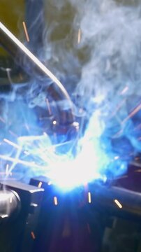 A mechanical marvel expertly crafts metal pipes on a factory floor. Brilliant blue arcs and golden sparks illuminate the argon welding process, showcasing modern industrial artistry.