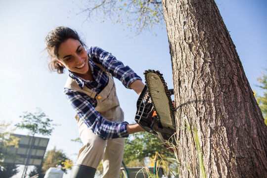 Woman on farm cuttiing tree with chain saw
