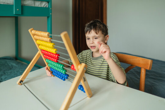 Focused boy learning mathematics with colorful abacus indoors