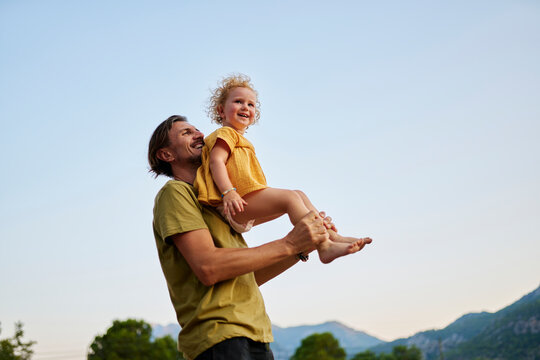Happy man lifting daughter standing by clear sky