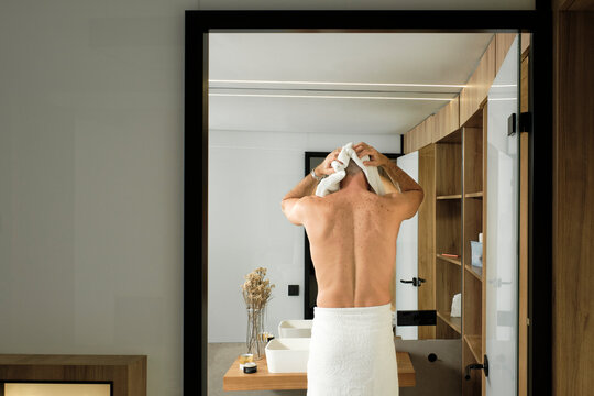 Mature man wearing towel drying hair in bathroom after shower at home