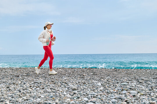 Jogging on a Mediterranean pebble beach in red sportswear