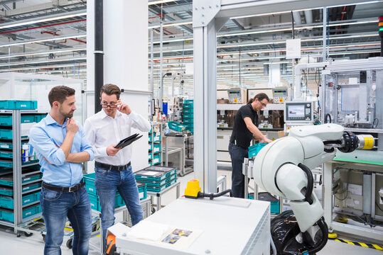Man operating assembly robot in factory and two men talking