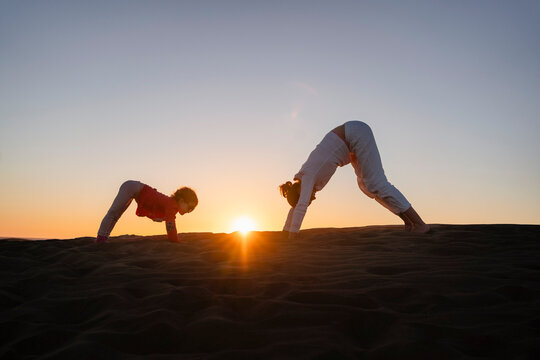 Mother and daughter practicing yoga in sand dunes at sunset, Gran Canaria, Spain