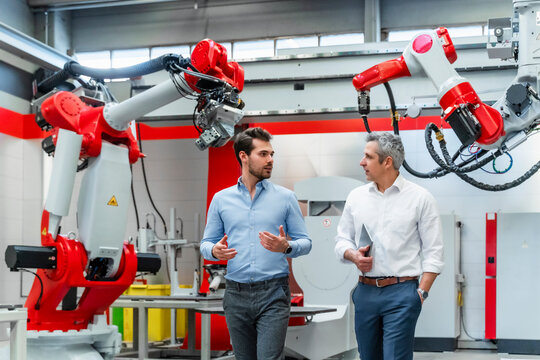 Young male automation engineer discussing with colleague against machinery in factory