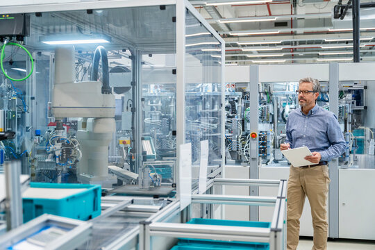 Employee with tablet inspecting industrial robots in modern factory