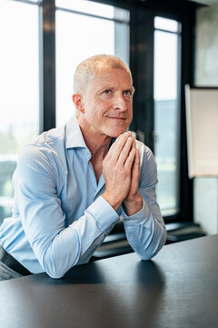 Smiling thoughtful executive leaning on desk in office