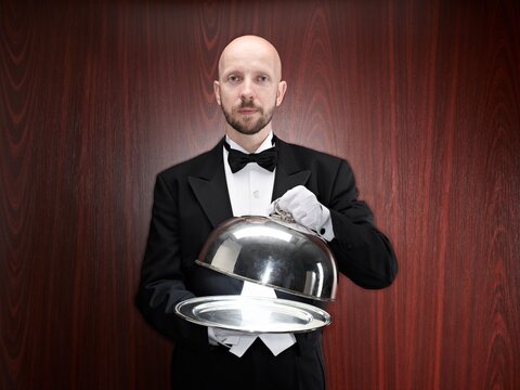 Butler in tuxedo presenting an empty silver tray with cloche