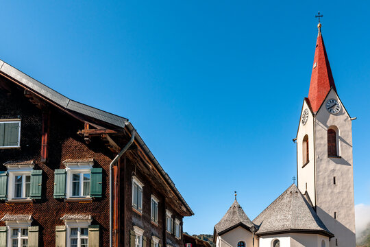 Historic Walserhaus and church under blue sky in Warth