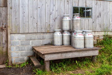 Obraz premium Milk Milk cans stacked beside a wooden building in a rural setting