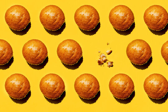 Pattern of rows of muffins against yellow background with single one missing