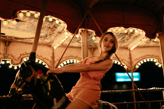 Smiling woman riding a carousel horse at an amusement park at night