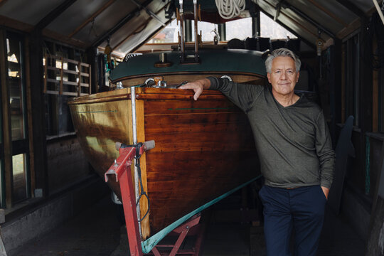 Portrait of a proud senior man at wooden boat in a boathouse
