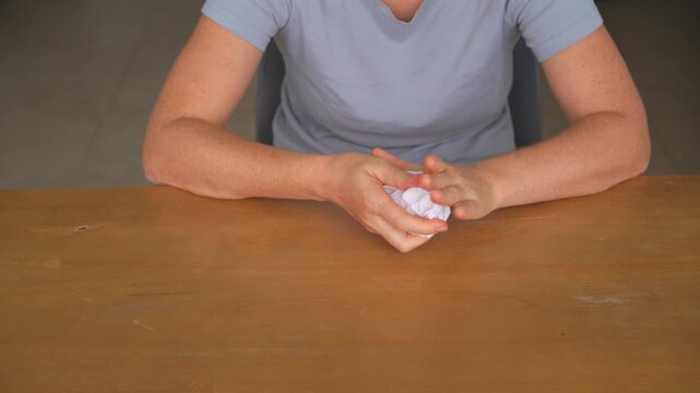 Woman crumpling two sheets of paper at a table, high quality audio recording. Crisp crunching sounds and expressive hand movement. Stress relief, frustration and everyday lifestyle concept.