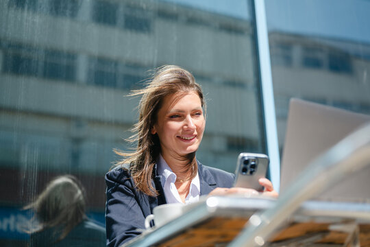 Smiling businesswoman using smartphone and laptop at outdoor cafe
