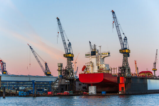 Large ship under repair in a Hamburg harbor dry dock at sunset