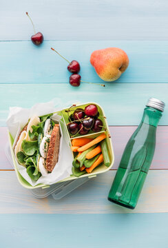 Healthy school food in a lunch box, vegetarian sandwich with cheese, lettuce, cucumber, egg and cress, sliced carrot and celery, cherries and pear