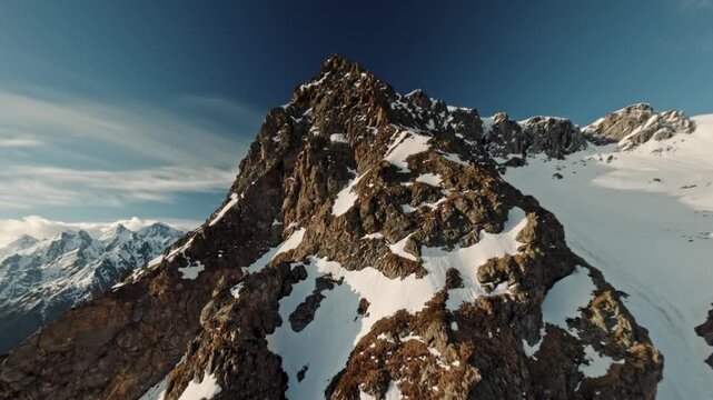 Aerial view flight climbing mountain summit cliff snow reversal dive from top ridge alpine landscape. High quality 4k footage