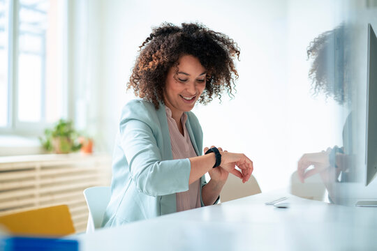 Smiling businesswoman with curly hair checking time on smart watch at office