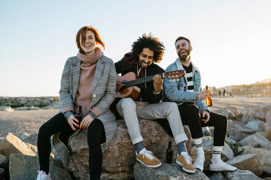 Three happy friends with guitar sitting outdoors at sunset