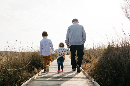 Back view of grandfather and grandchildren strolling hand in hand on boardwalk