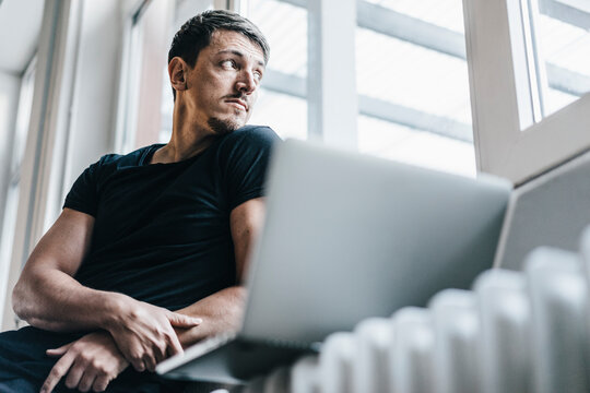Man sitting on heater with laptop
