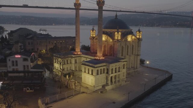Aerial view of the illuminated Ortak&ouml;y Mosque on the shores of the Bosphorus in Istanbul, Turkey, with the iconic Bosphorus Bridge in the background.