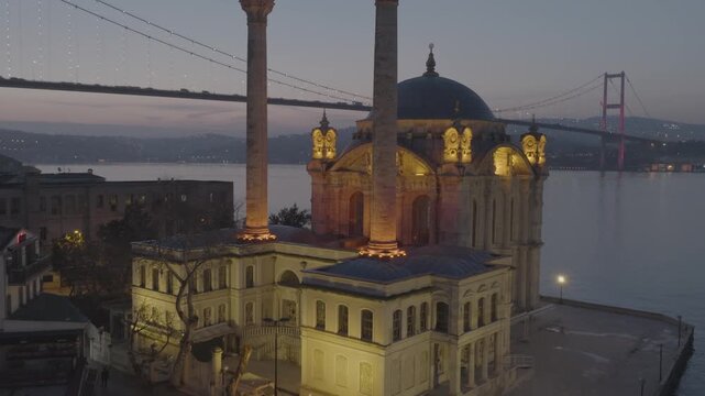 Aerial view of the illuminated Ortak&ouml;y Mosque on the shores of the Bosphorus in Istanbul, Turkey, with the iconic Bosphorus Bridge in the background.