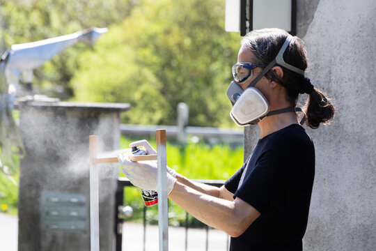 Hobbyist spray painting a wooden frame outdoors with respirator